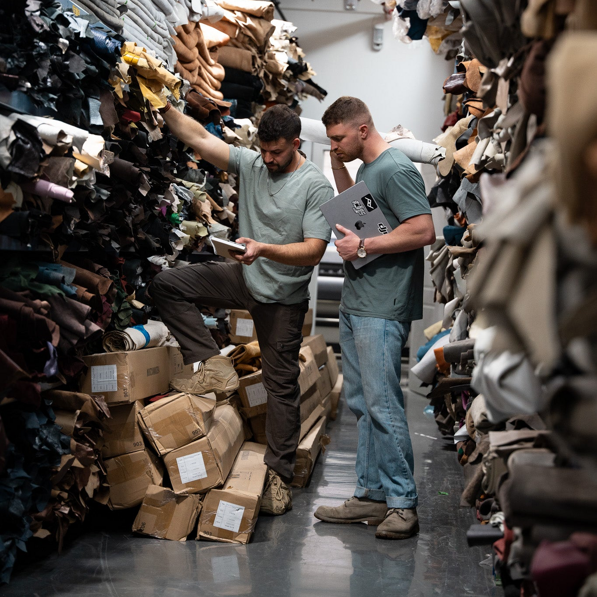 Two men checking stacked rolls of Italian leather in a leather warehouse