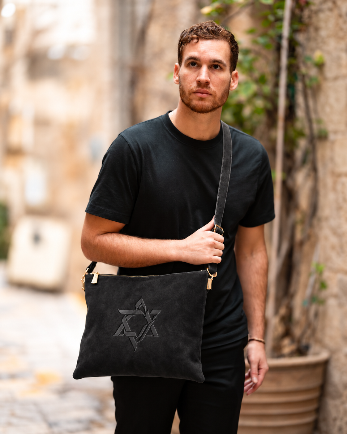 Man in a black shirt carrying the black Magen David leather tallit bag outdoors
