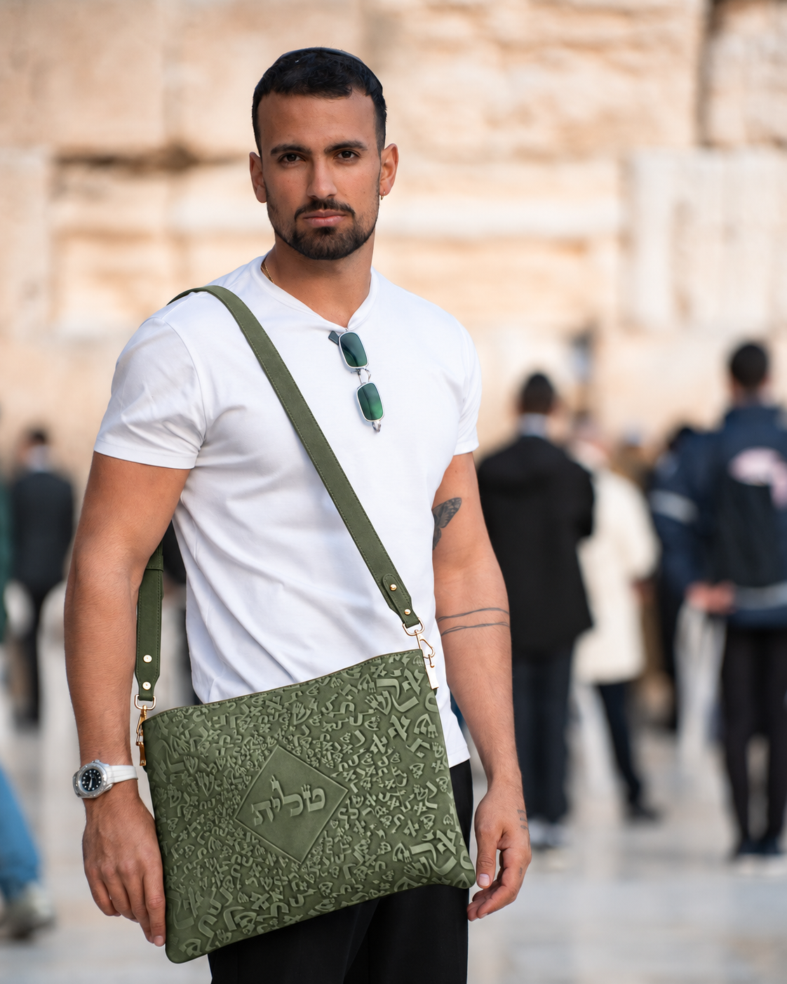 Man in a white shirt carrying the green leather tallit bag across his shoulder