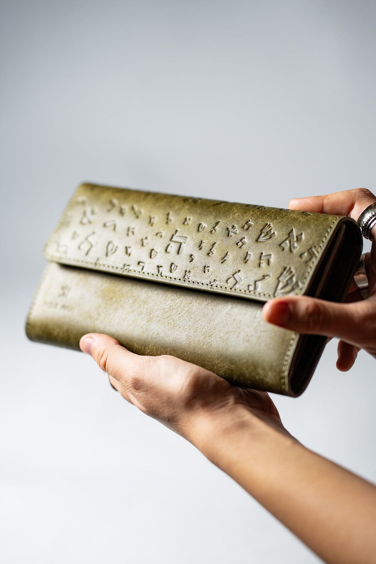 Hand holding the closed green embossed leather wallet