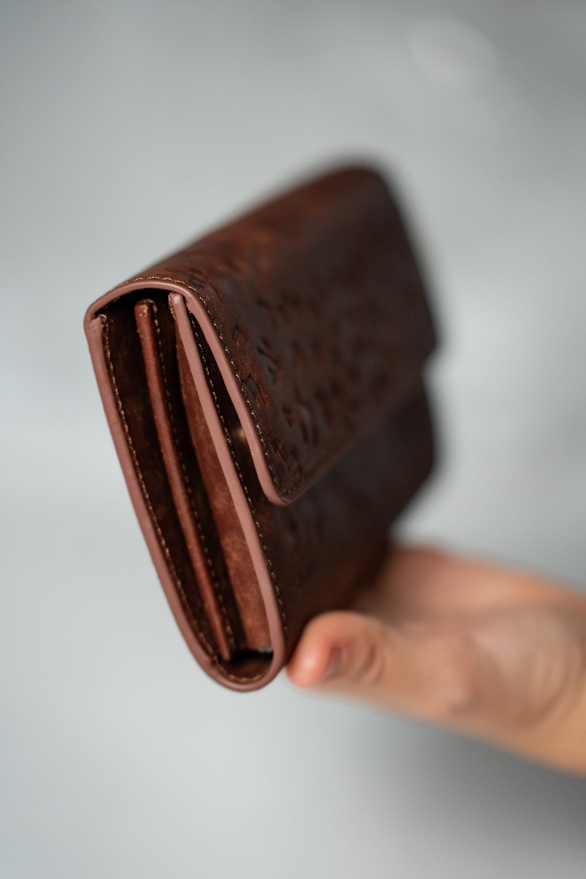 Hand holding the brown leather wallet, side view
